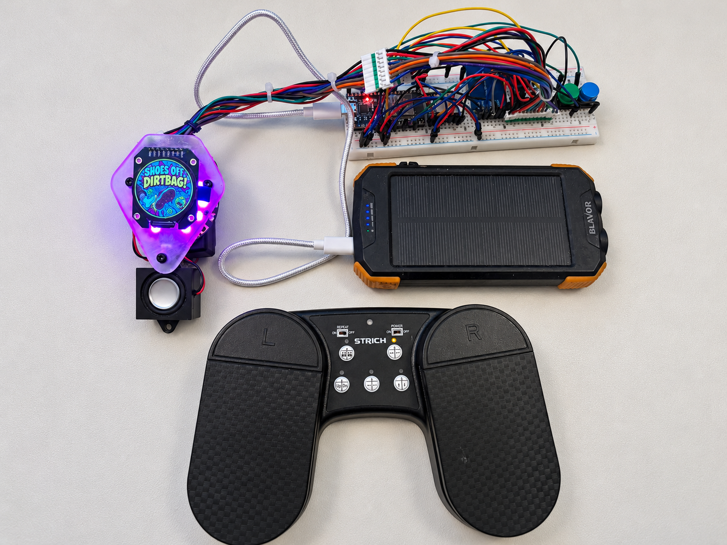 Shoes Off, Dirtbag assembled on my desk, with a purple light halo, round screen, speaker, wired breadboard, power bank, and Bluetooth foot pedal
